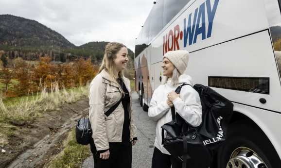 To damer som står og snakket utenfor en buss i høstlandskap