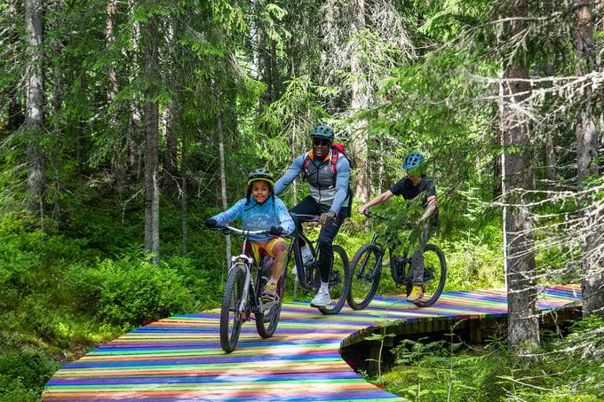 Familie sykler over trebru malt i regnbuens farger