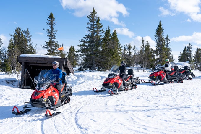 gruppe på fire på hver sin scooter, parkert utenfor gapahuk 